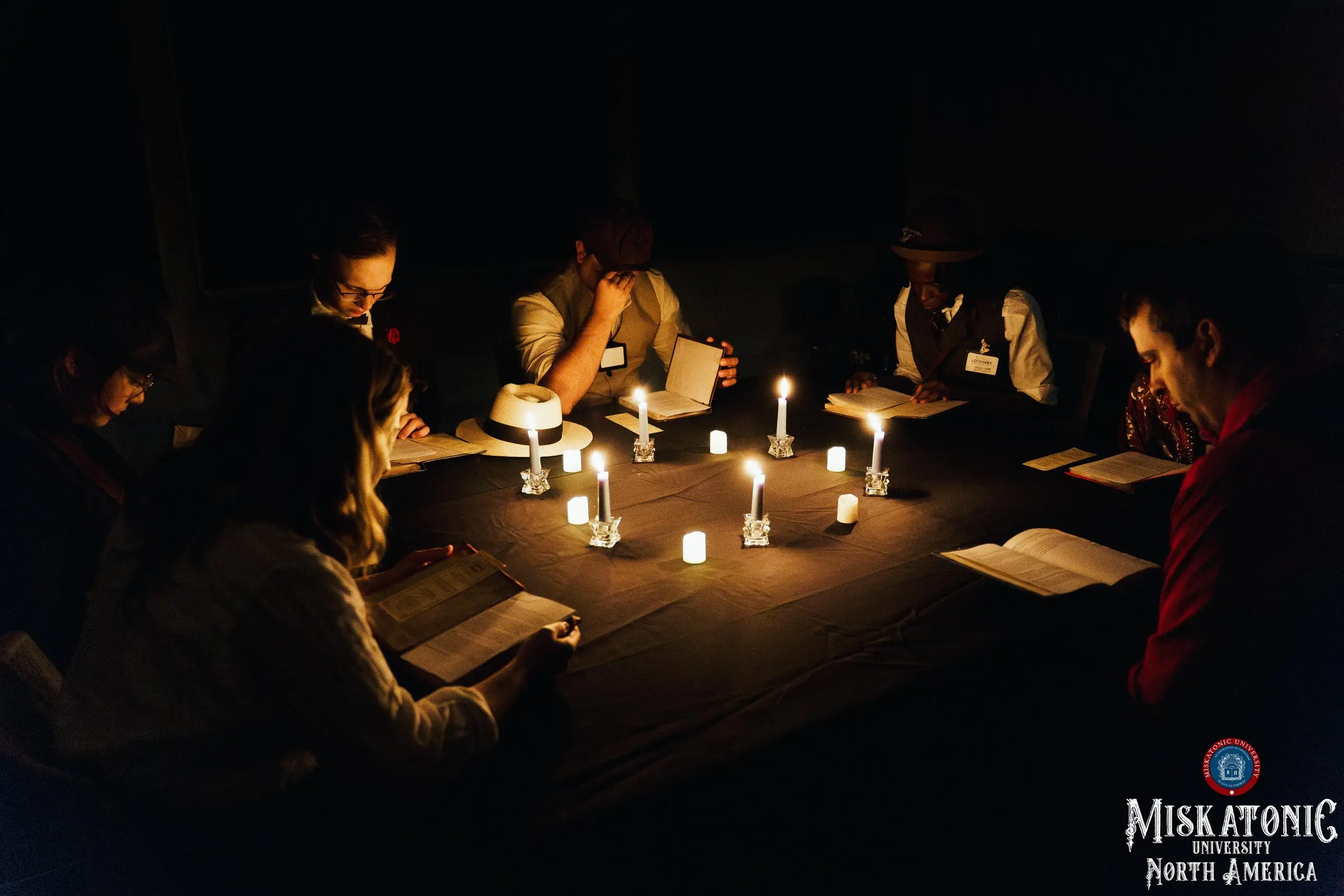 Three scholars bent over their books around a ring of candles
