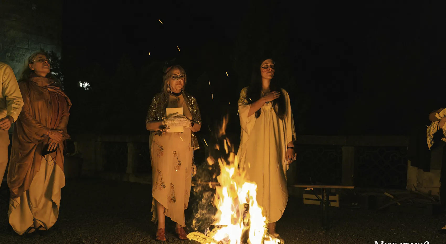 Figures in white gathered around a bonfire at night