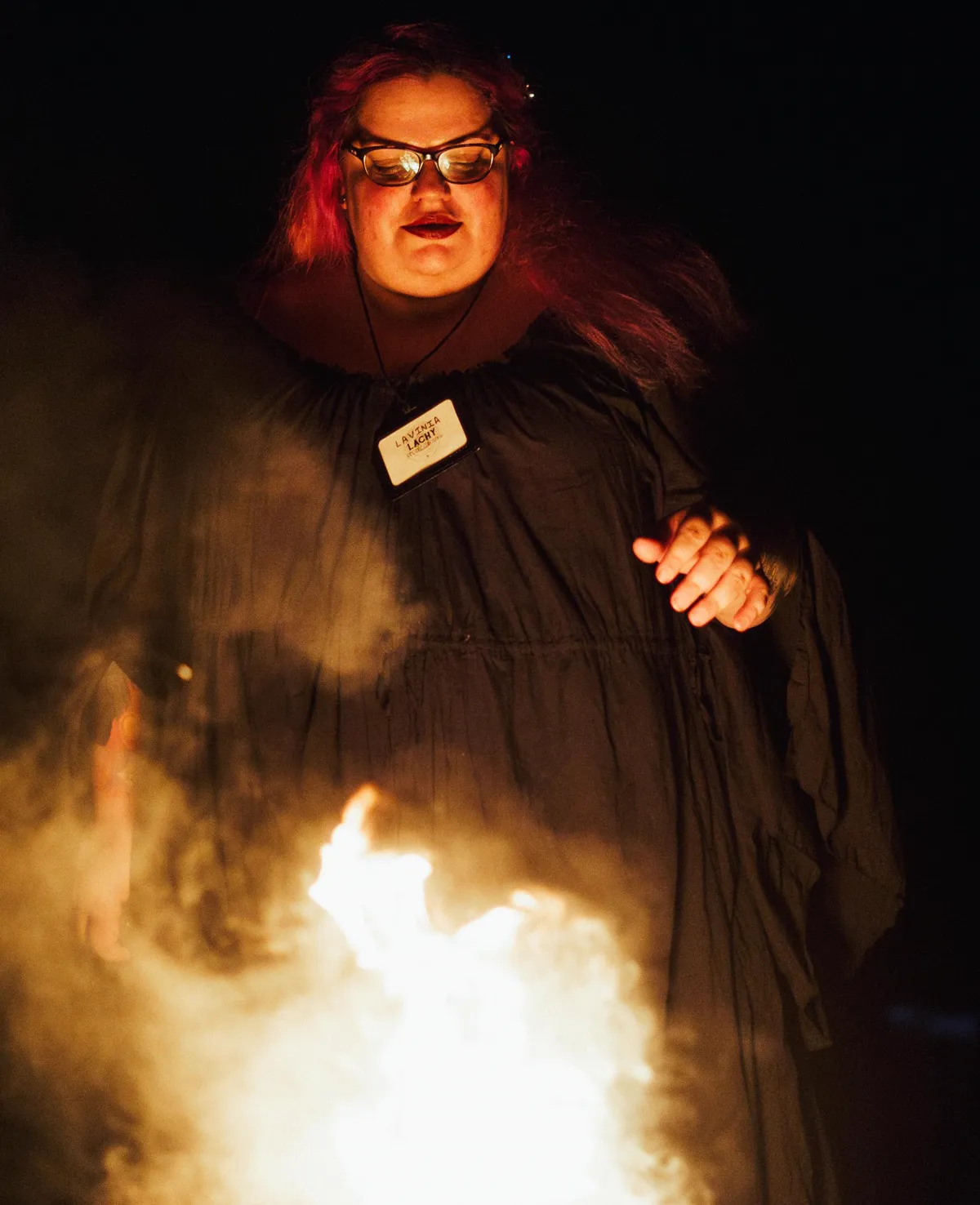 A robed figure stands over a fire