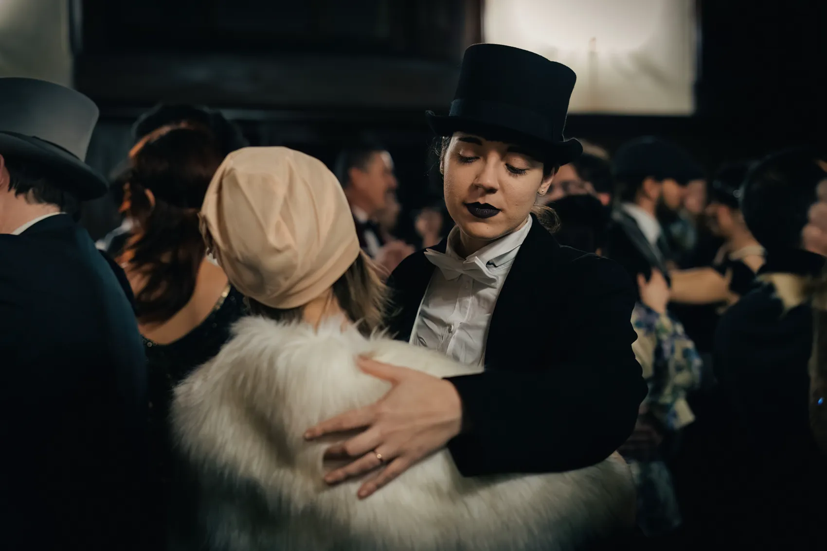 A figure in a top hat holds a friend close in the crowd