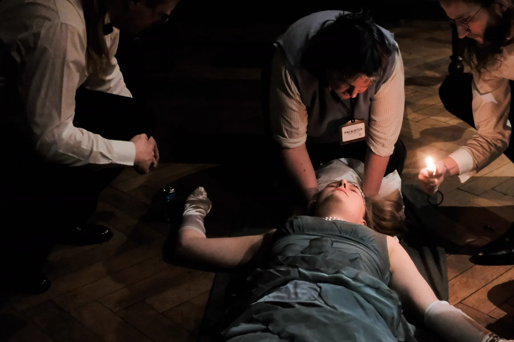 Scholars examine a woman lying on the floor by candlelight