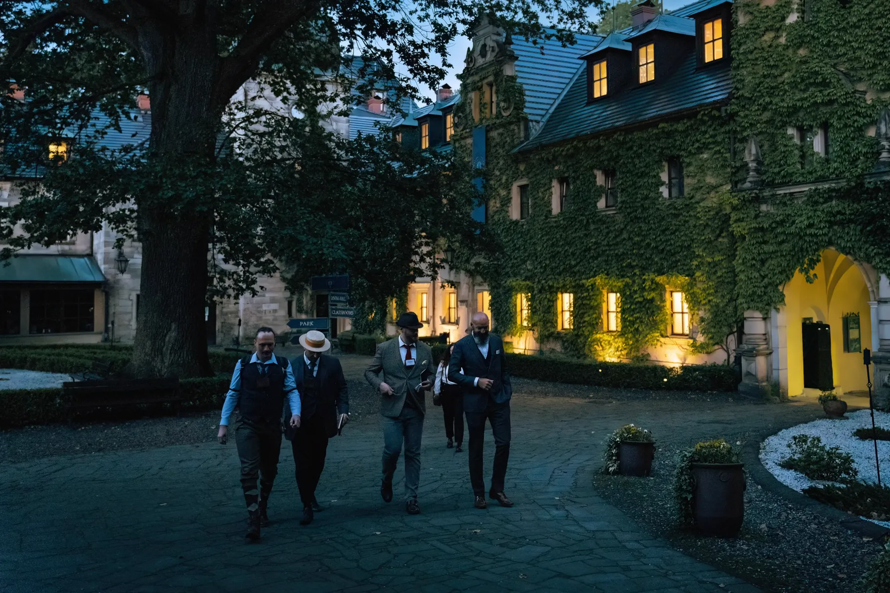 Scholars cross the castle courtyard at dusk, its windows already lit