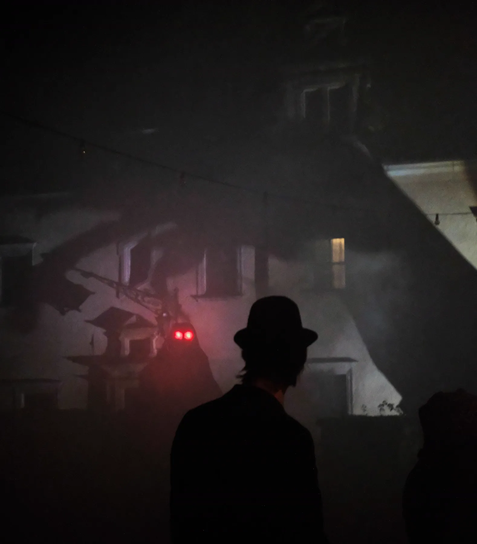 A man in a bowler hat stands in the fog before a figure with two red eyes