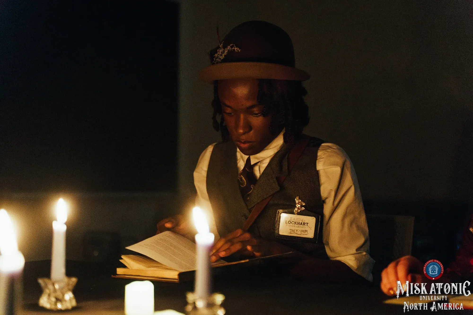 A student in a bowler hat reads by candlelight