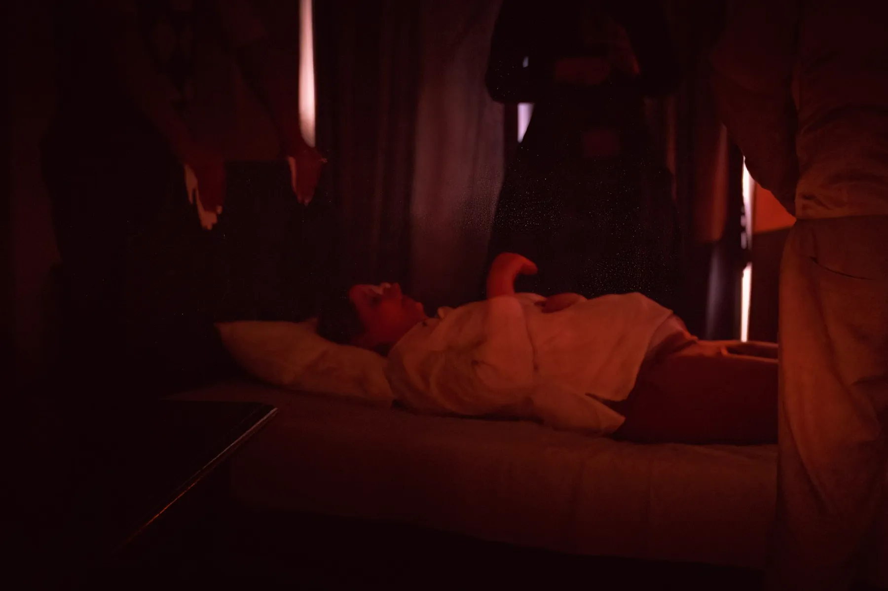 A sleeper lies on a bed bathed in red light