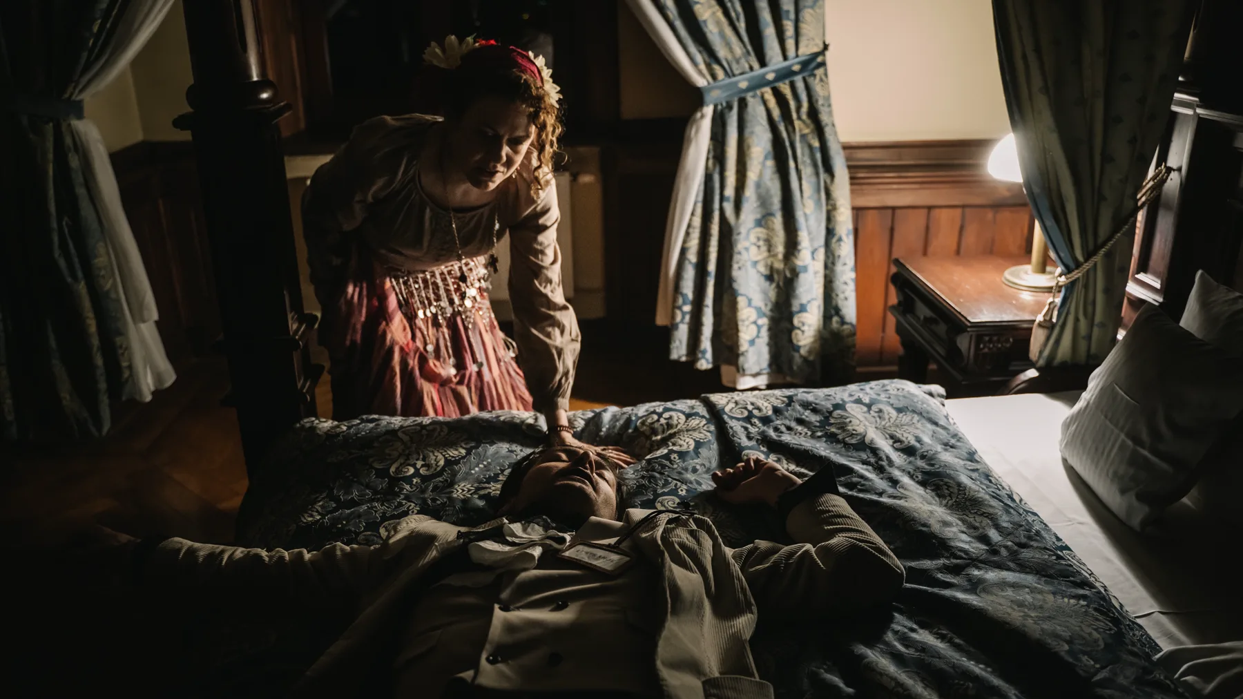 A woman bends over a sleeper in a canopy bed