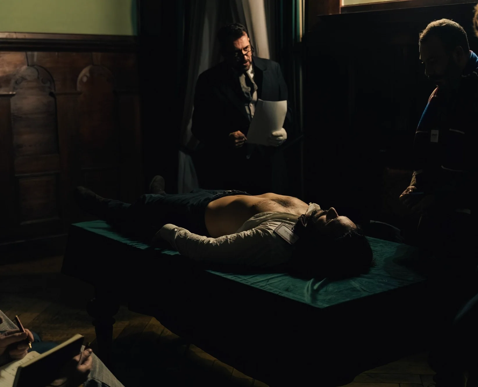 Scholars stand around a body laid out on a table, one of them reading from a sheet
